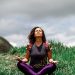 A woman enjoys peaceful meditation in a grassy field under a cloudy sky in Brazil.