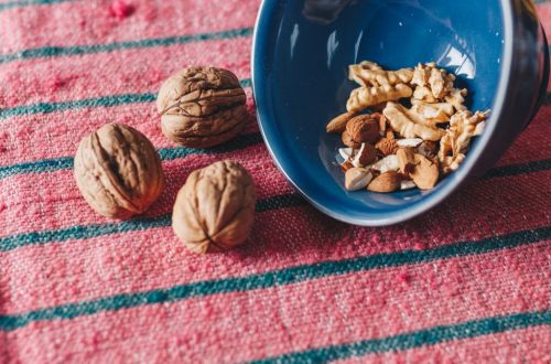 A variety of nuts, including almonds and walnuts, spilled from a blue bowl onto a pink textile surface.