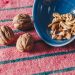 A variety of nuts, including almonds and walnuts, spilled from a blue bowl onto a pink textile surface.